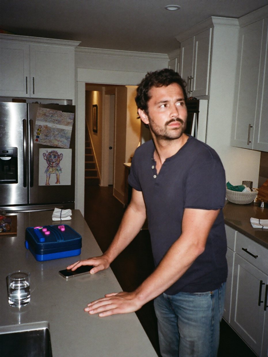 Illustrative evening scene: a father pauses at the kitchen counter, with school things still out.