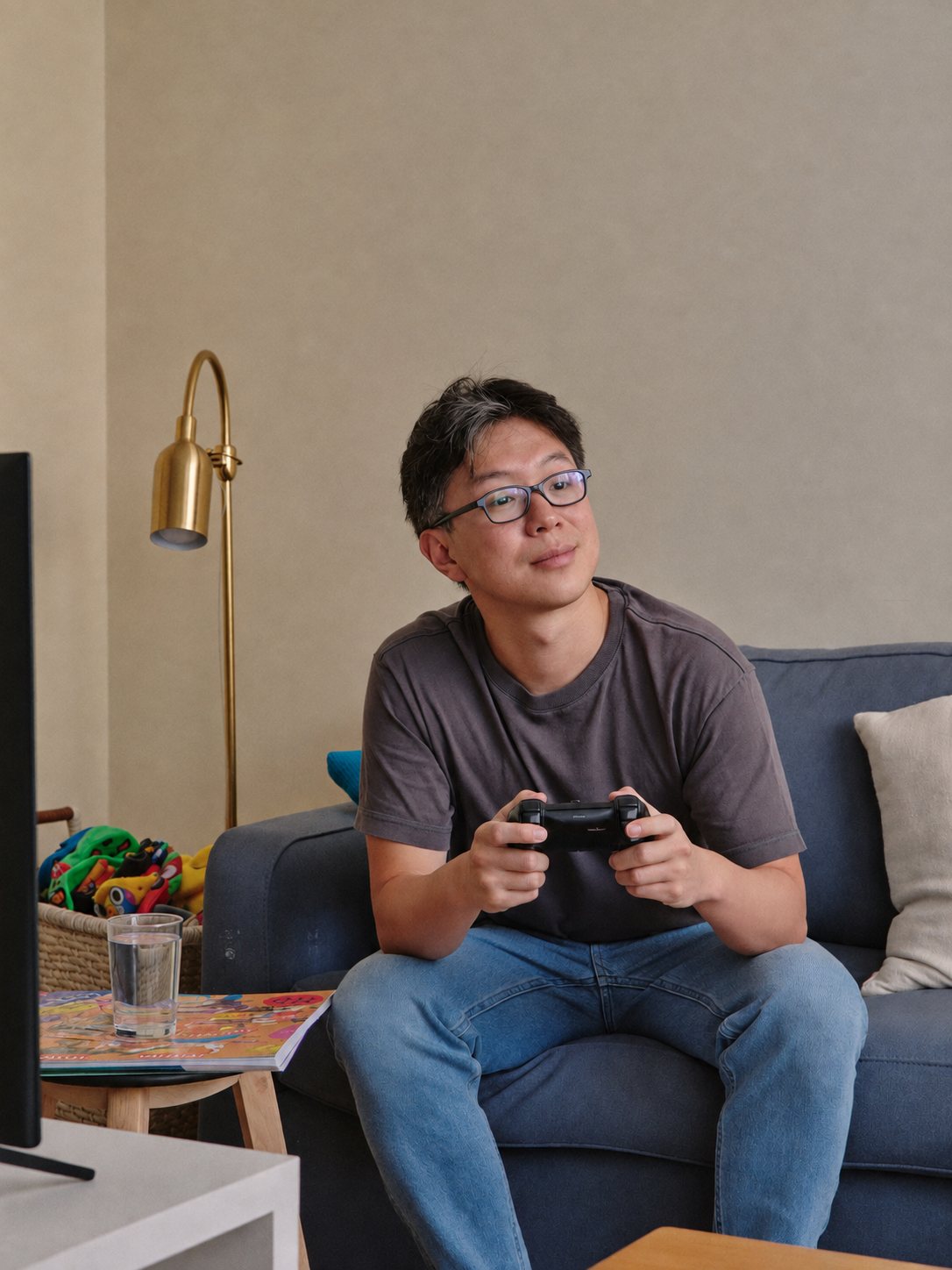 A dad with glasses sitting on the couch holding a game controller.